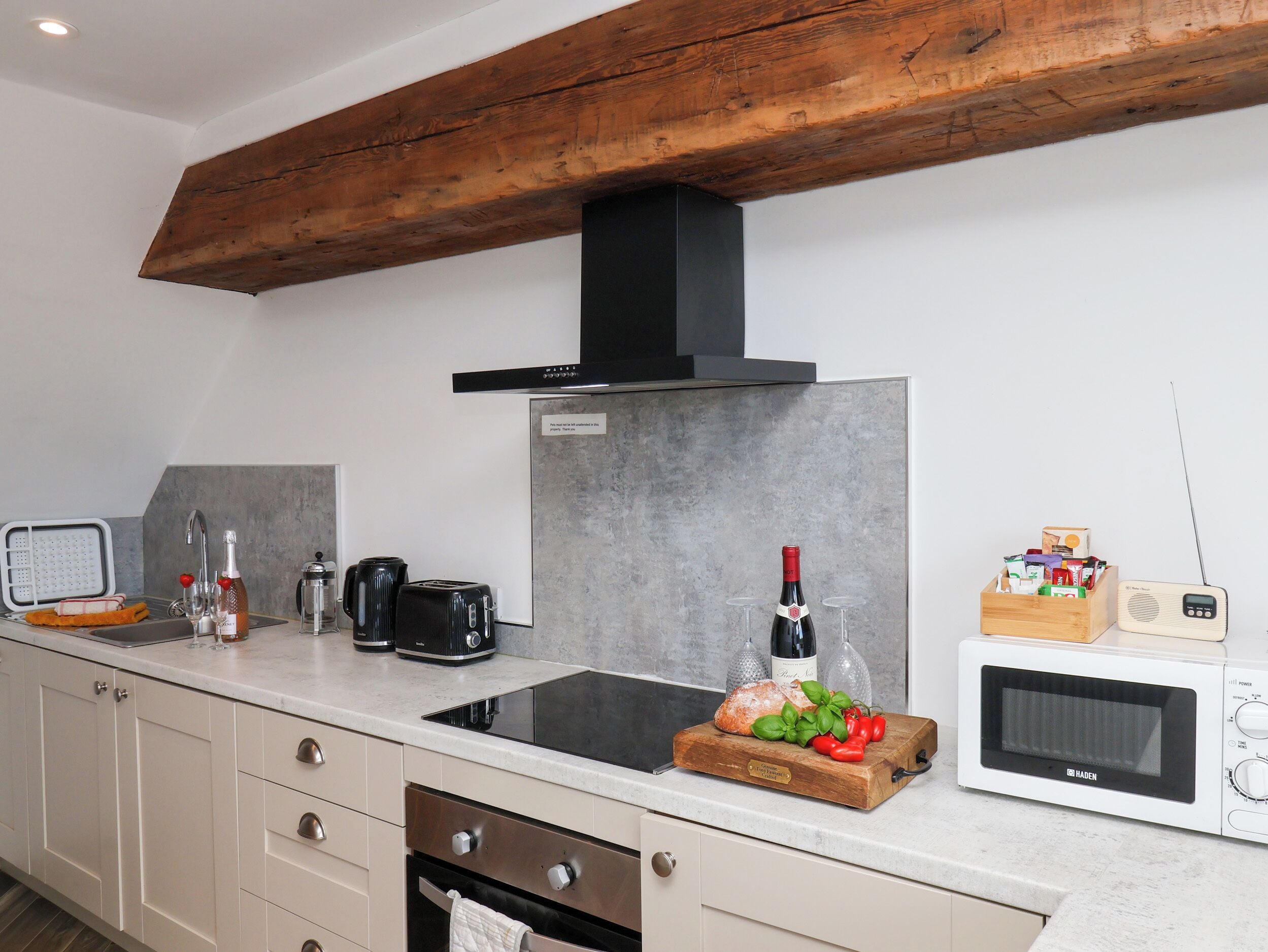 A modern kitchen with a built-in stove, a microwave, a toaster, and a wooden cutting board with bread and tomatoes.