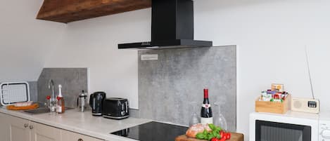 A modern kitchen with a built-in stove, a microwave, a toaster, and a wooden cutting board with bread and tomatoes.