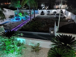 Un’area di parcheggio con diverse automobili, un giardino curato con palme e un edificio sullo sfondo.