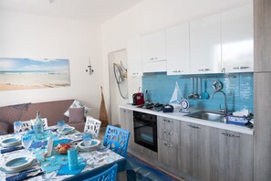 Una cucina moderna con schienale blu, mobili bianchi e un'area pranzo con tavolo apparecchiato per due.