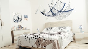 Un dormitorio con cama, mesita de noche, repisa en la pared con objetos decorativos y una hamaca colgante.