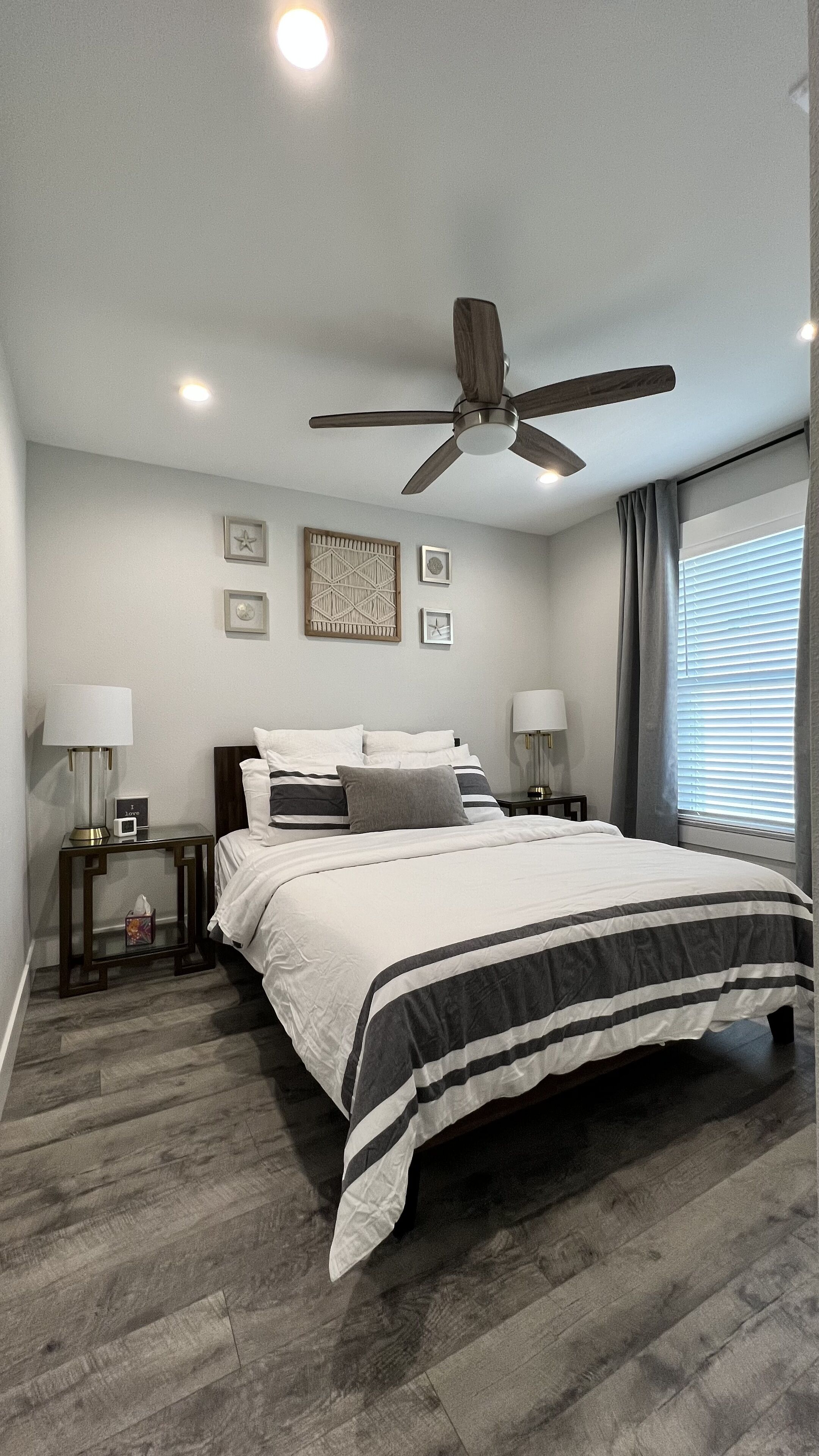 A bedroom with a bed, two bedside tables, a ceiling fan, and a window with curtains.