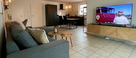 A modern living room with a grey sofa, a coffee table, and a TV displaying a man.