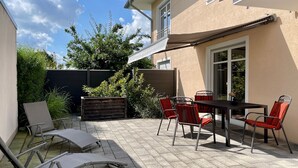 A patio with a table and chairs, a covered area, and a view of a building. - Boardinghouse - Apartment (Lippstadt)