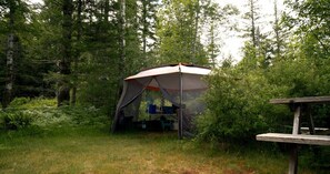 A tent set up in a forested area with a picnic table nearby.