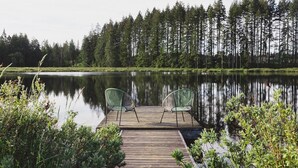Un muelle de madera con dos sillas mirando a un lago tranquilo, rodeado de un bosque denso.