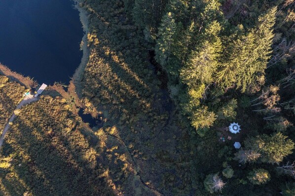 An aerial view of a forested area with a small clearing, a circular structure, and a pathway leading to a building.