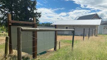 Un espace délimité par une clôture, avec un portail en métal, un poteau en bois et, au fond, un bâtiment doté d’un toit en métal.