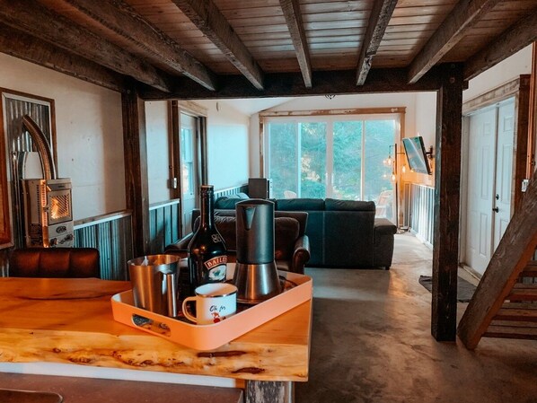 Un salon chaleureux avec un plafond en bois, une table basse sur laquelle se trouve un plateau avec divers objets, un canapé et une vue dégagée sur l’extérieur grâce à une grande fenêtre.