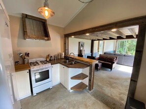 Une cuisine de taille réduite, équipée d’une cuisinière à gaz, d’un évier et d’étagères en bois.