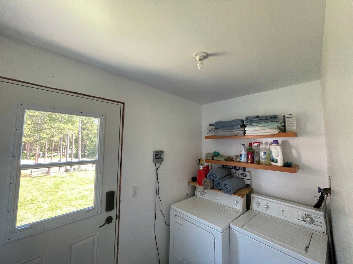 A laundry room with a washing machine, dryer, and shelves with folded clothes and cleaning supplies.