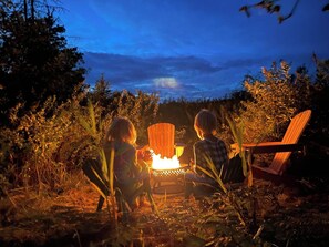 Two people sitting on chairs around a campfire in a natural setting. - Tiny house & Bubble Sauna on Lakefront Farm Oasis (Merville)
