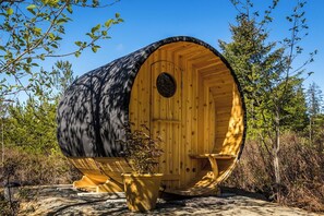 Una estructura cilíndrica de madera con una puerta, rodeada de árboles.