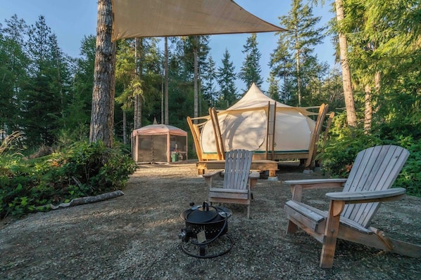 A campsite with two tents, a fire pit, and two Adirondack chairs.