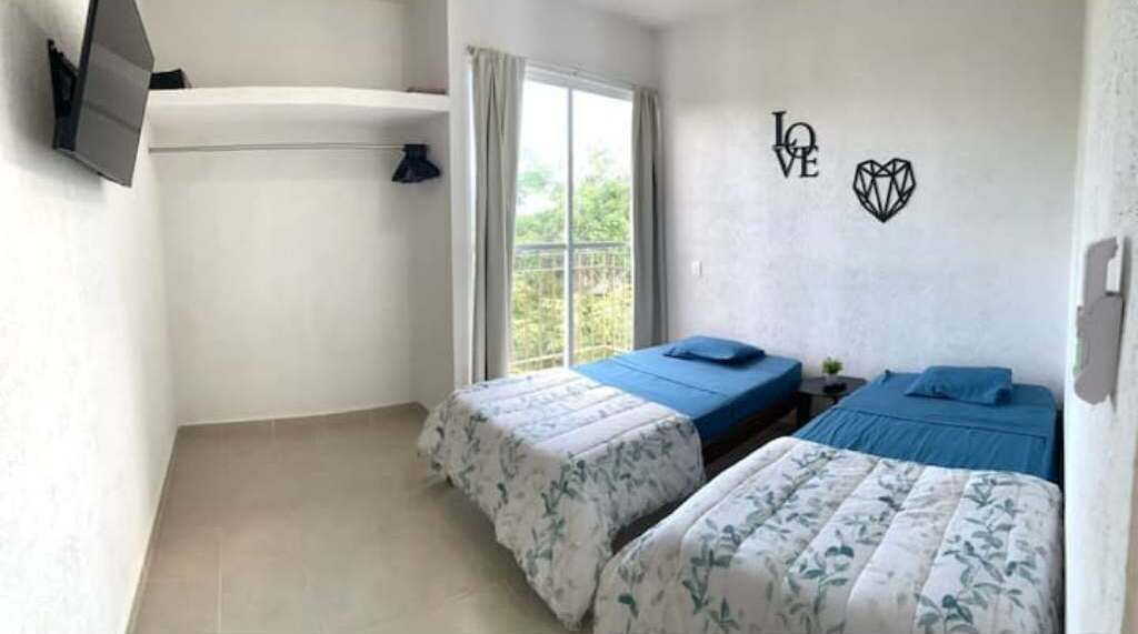 A room with two beds, a TV mounted on the wall, and a window with curtains.