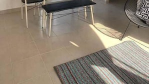 Een kamer met een eettafel, stoelen, een bankje, een stoel met een gestreept kussen, een spiegel en een raam met gordijnen.