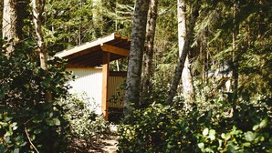 A forested area with a small wooden structure labeled "Outhouse." - Lake Front Farm, Glamping & Sauna Experience (Merville)
