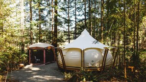 A forested area with two tents, one larger and one smaller, connected by a path.