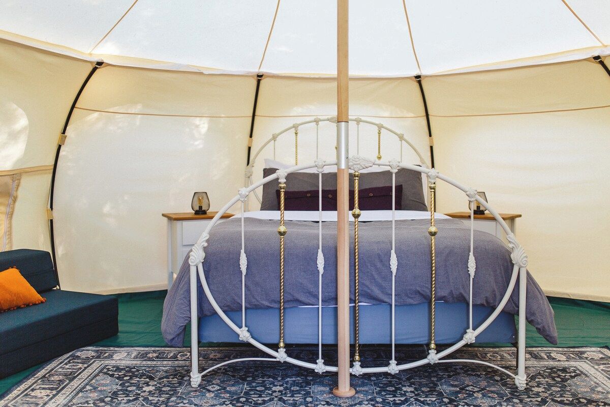 Une tente circulaire avec un lit placé au centre, entouré d’un tapis à motifs.