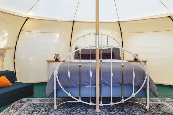 A circular tent with a bed centered in the middle, surrounded by a patterned rug.