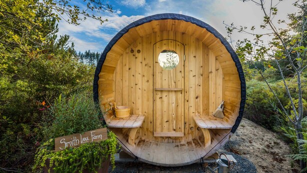Een houten sauna met een ronde deur, twee banken en een bord waarop 'Smith Lake Farm' staat.