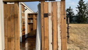 Een houten constructie met een metalen deur, een plank met flessen en een houten bank.