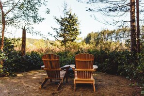 Two wooden Adirondack chairs facing each other with a table between them, set in a forested area.