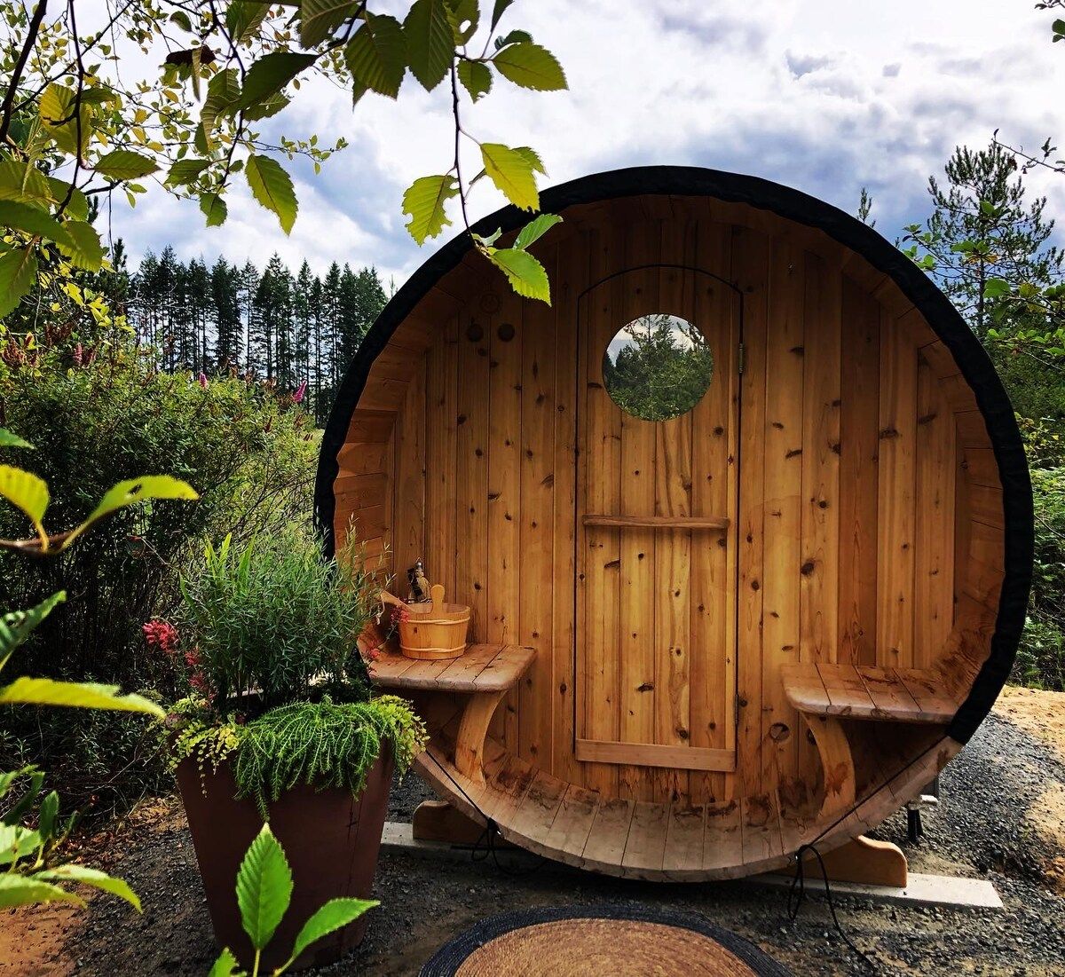 Una struttura a forma di botte in legno con una panca all'interno, immersa nel verde.