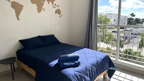 Un dormitorio con una cama grande, un mapa del mundo en la pared y vistas a un estacionamiento a través de una ventana.