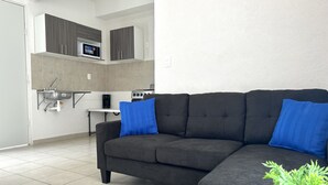 Una sala moderna con un sofá seccional gris oscuro, dos cojines azules, una mesita y una planta en maceta.