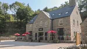 A stone building with a chimney, multiple windows, and outdoor seating with red umbrellas.