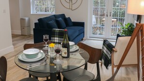 A dining area with a glass table, chairs, a bottle of wine, and a blue sofa in the background.