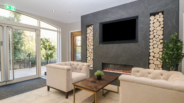 A modern lobby with a fireplace, comfortable seating, and a large TV screen.