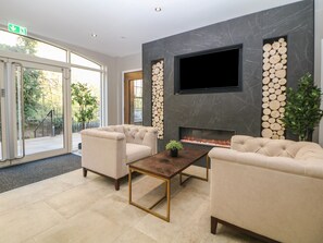 A modern lobby with a fireplace, comfortable seating, and a large TV screen.