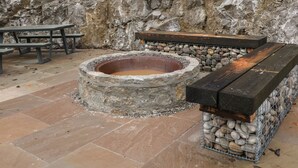 A stone fire pit with a metal grill, surrounded by stone walls and a tiled floor.