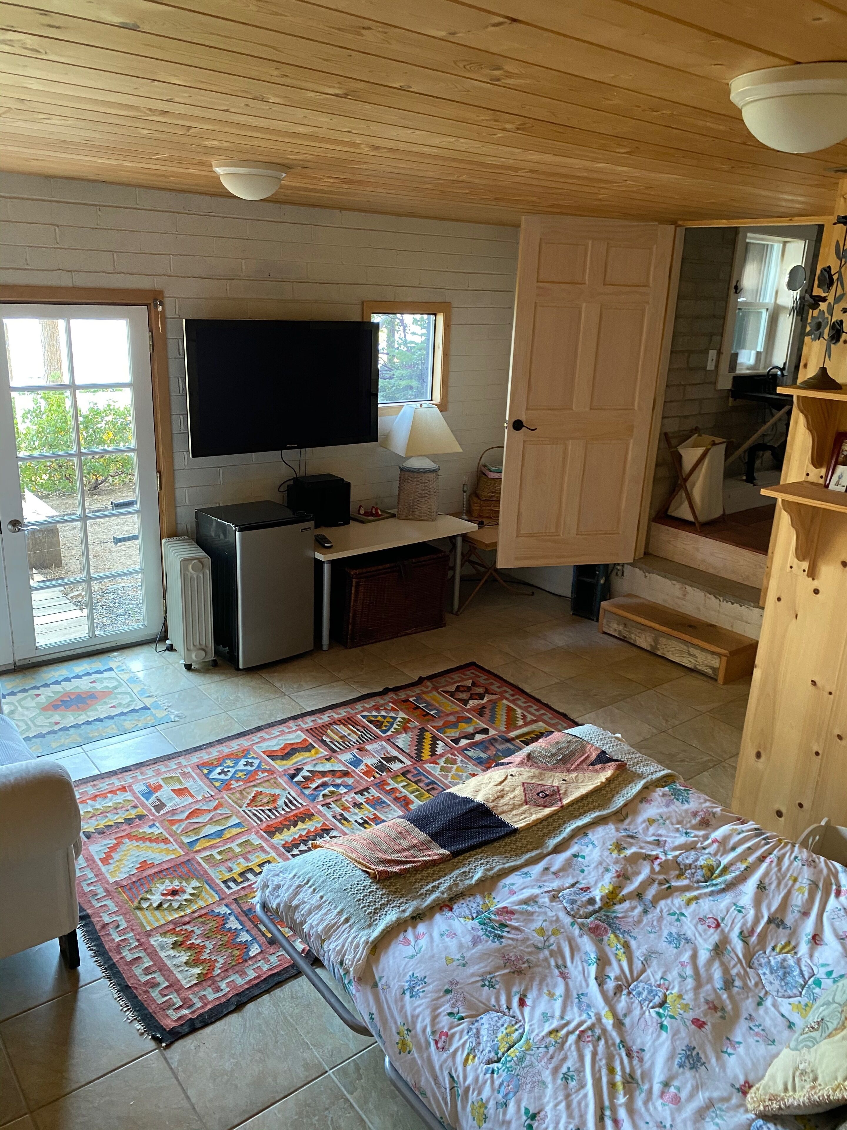 A bedroom with a bed, a desk, a television, and a window.