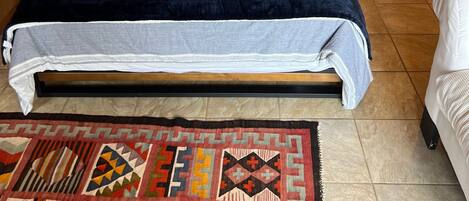 A wooden-paneled bedroom with a bed, two decorative pillows, a nightstand, a red side table, a patterned rug, and a staircase leading to an upper level.