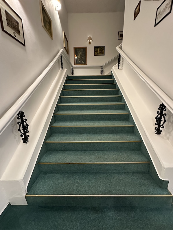 A staircase with green carpeted steps, white walls, and black balusters.