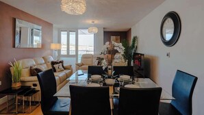 A modern living room with a glass dining table, black chairs, a beige sofa, and a large mirror on the wall. - Marina with a view / 2 bd flat (Brighton and Hove)