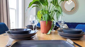 A dining table with black plates, a knife, and a fork, a potted plant, and two wine glasses. - Sea Breeze - 1 bedroom flat (Brighton and Hove)