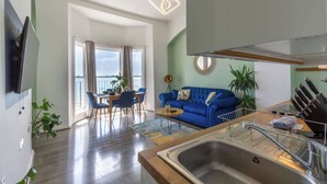 A modern living room with a blue sofa, dining area, and a kitchen with a sink. - Sea Breeze - 1 bedroom flat (Brighton and Hove)