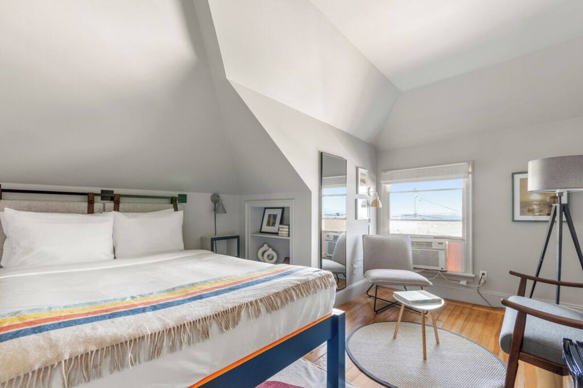 A bedroom with a large bed, a chair, a small table, and a window with a view.