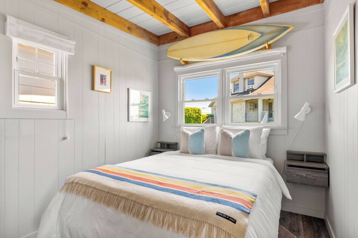 A bedroom with a bed, a window with a view, and a surfboard hanging on the wall.