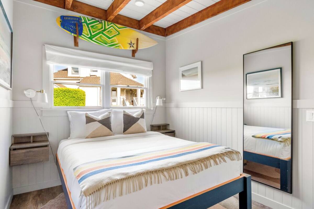 A bedroom with a bed, bedside tables, a window with a view, and a ceiling with wooden beams.