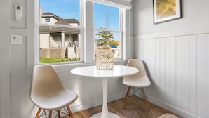 A room with a white table and two chairs, a window with a view of a house and a tree, and a framed picture on the wall. - The Inn Spot (Hampton Bays)