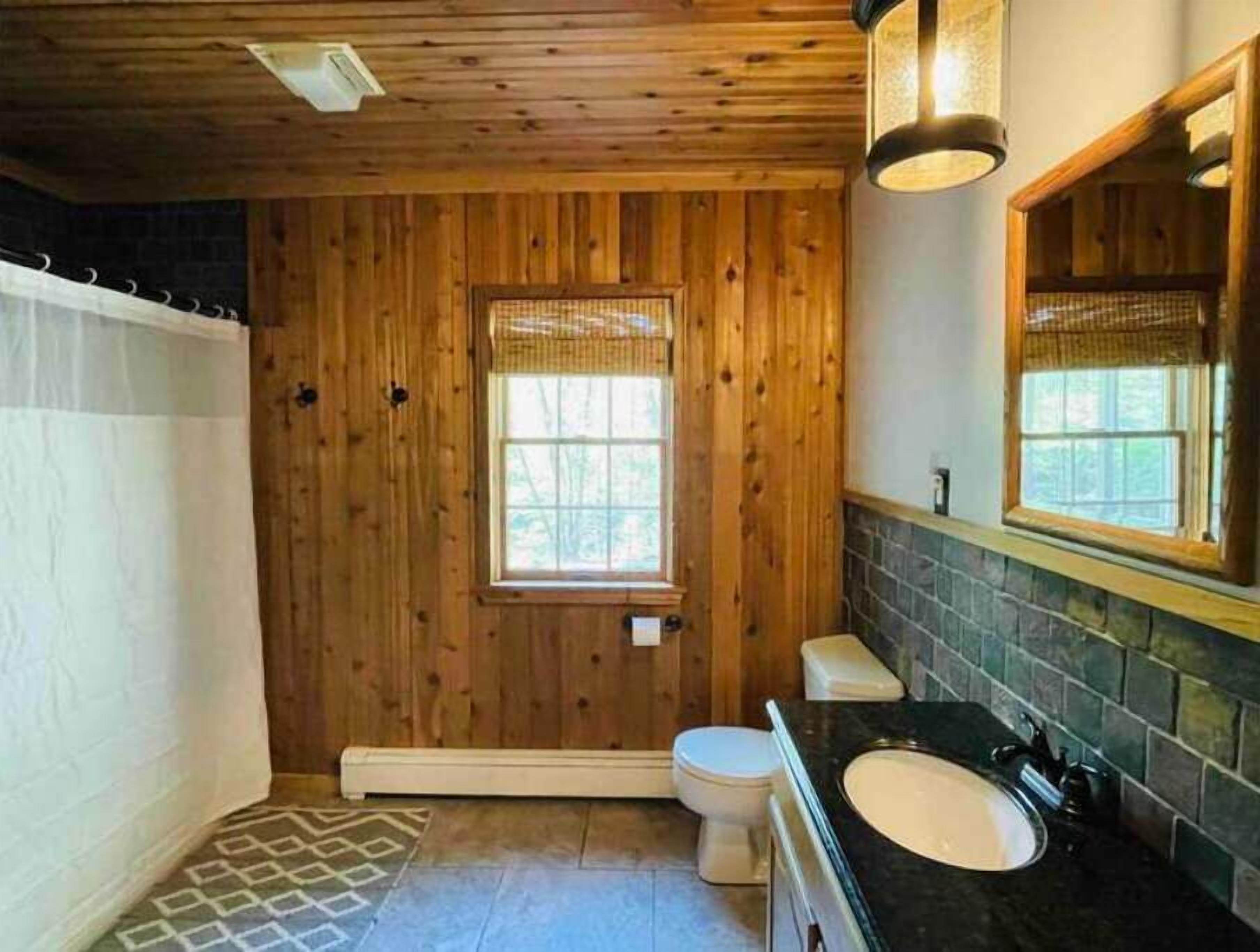 Ein Badezimmer mit Holzwandverkleidung, einem Fenster, einer Toilette und einem Waschbecken.