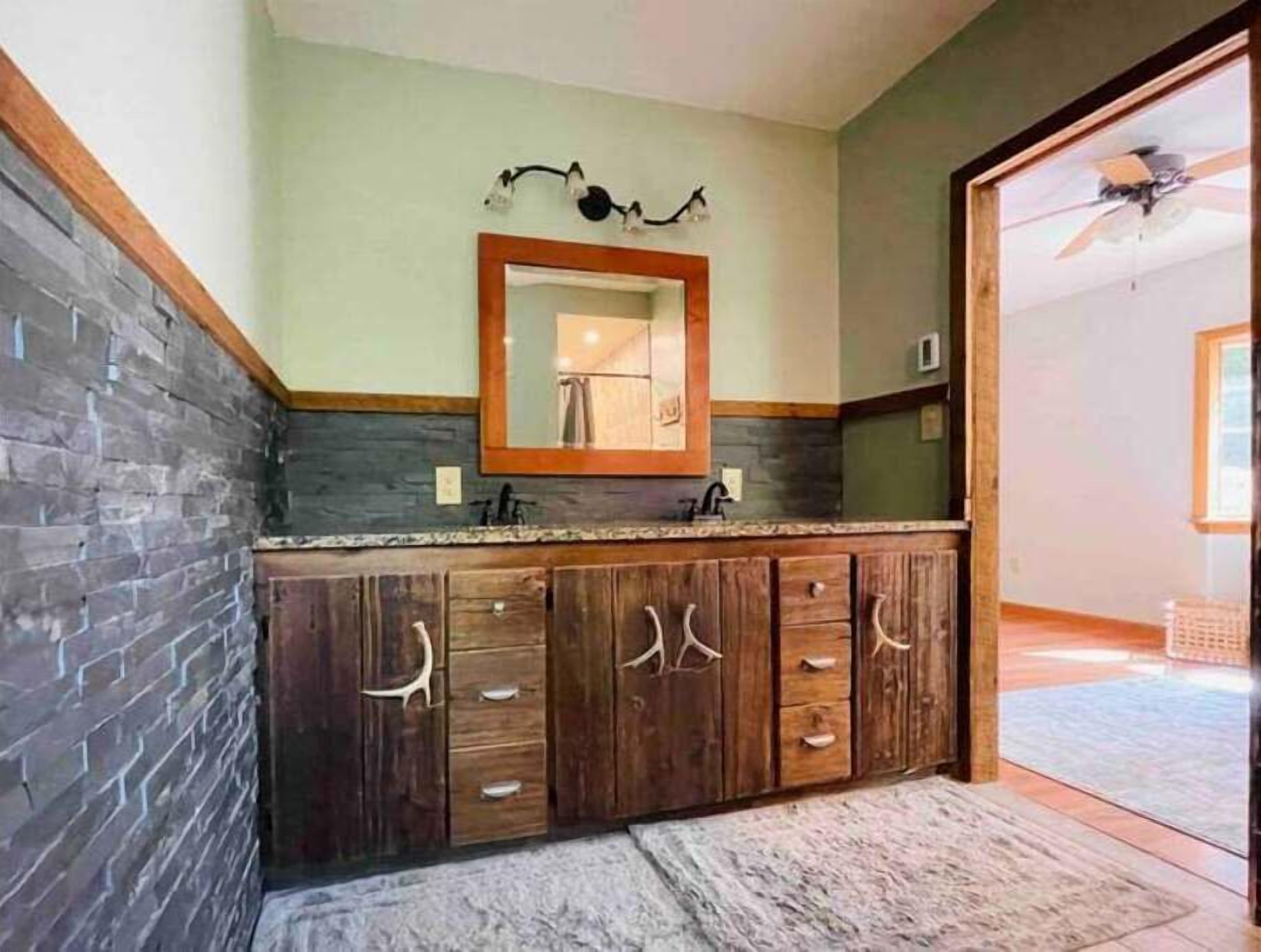 Une salle de bain avec un mur en pierre, un meuble-lavabo en bois et un ventilateur de plafond.