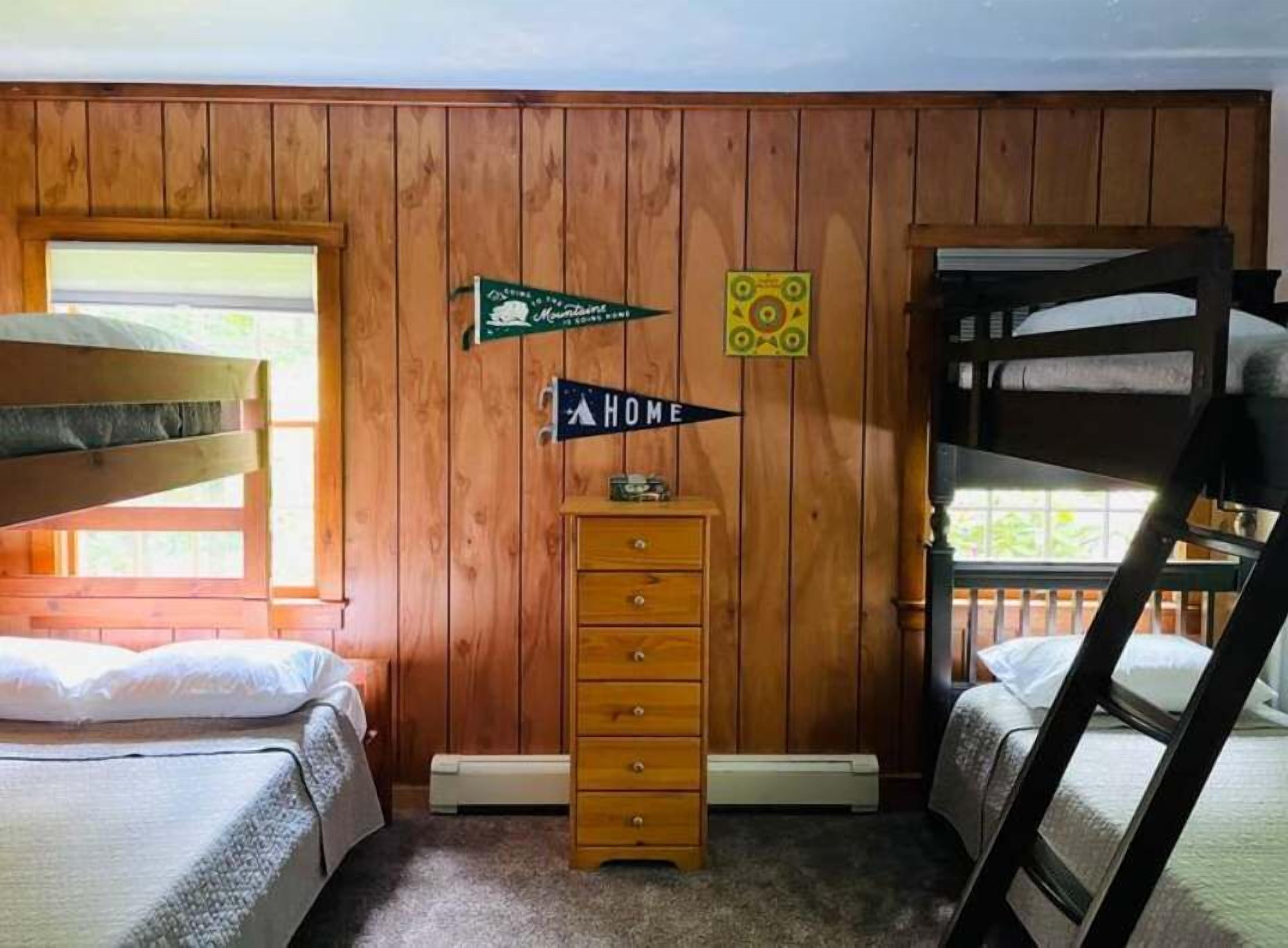 A cabin-style room with wooden walls, bunk beds, a dresser, and a sign indicating the room's name.