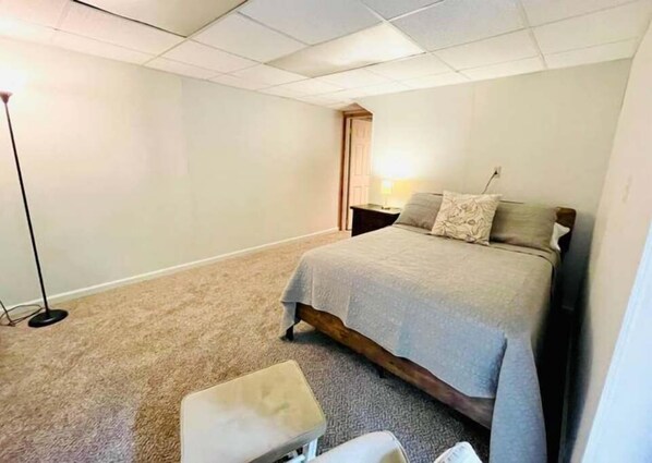 A bedroom with a bed, a nightstand, a lamp, and a carpeted floor.