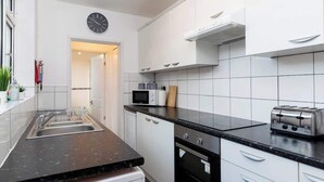 Una cocina moderna con armarios blancos, una encimera negra, microondas, tostadora y un reloj en la pared.